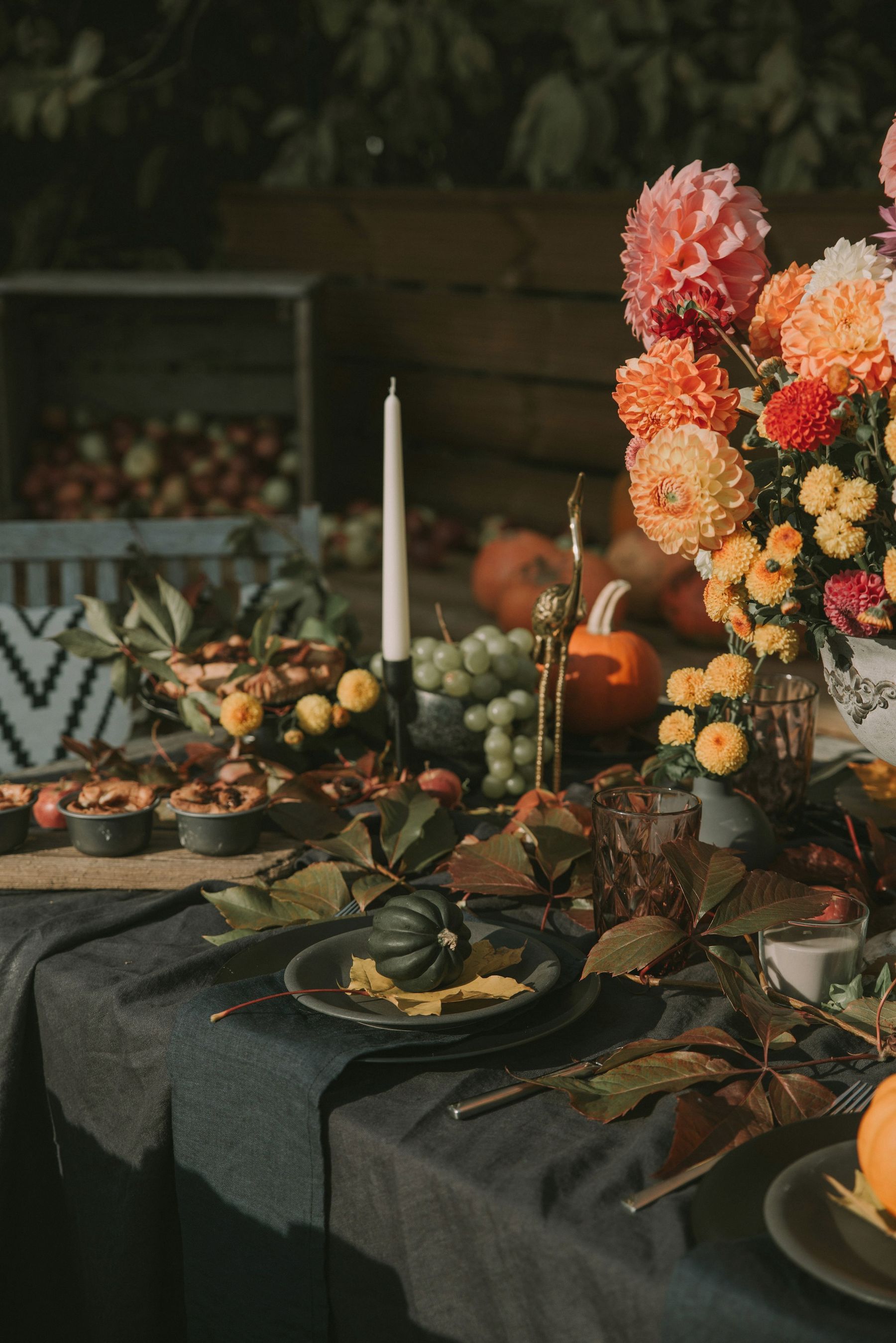 An autumn table centerpiece of dahlias, candles and seasonal fruit