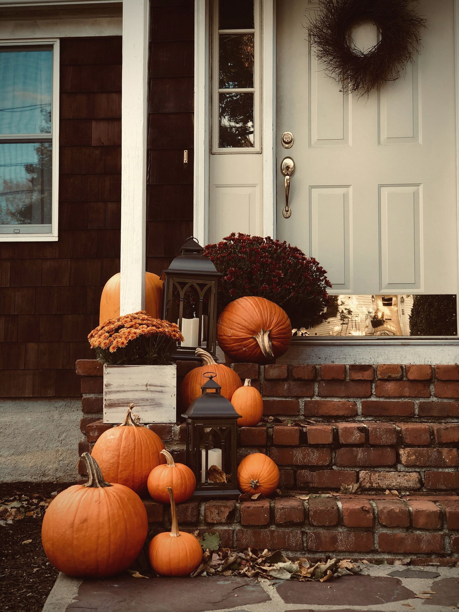 A brick stoop with lanterns, pumpkins and a wreath on the door