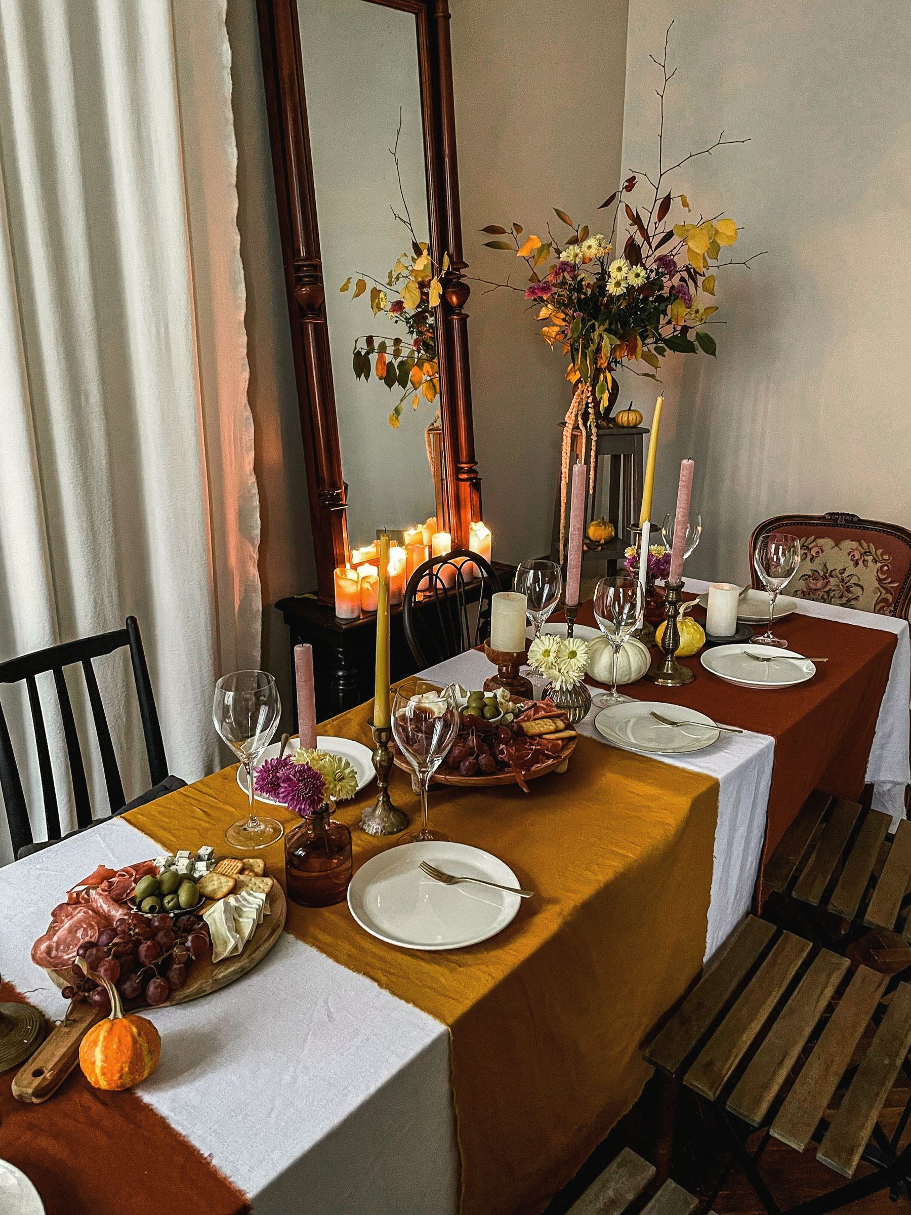 A long dining table set for an autumn dinner with candles and a mustard runner