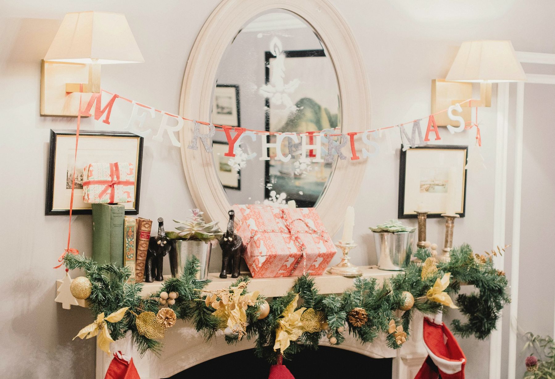 A mantel with garland, wrapped gifts and a Merry Christmas banner