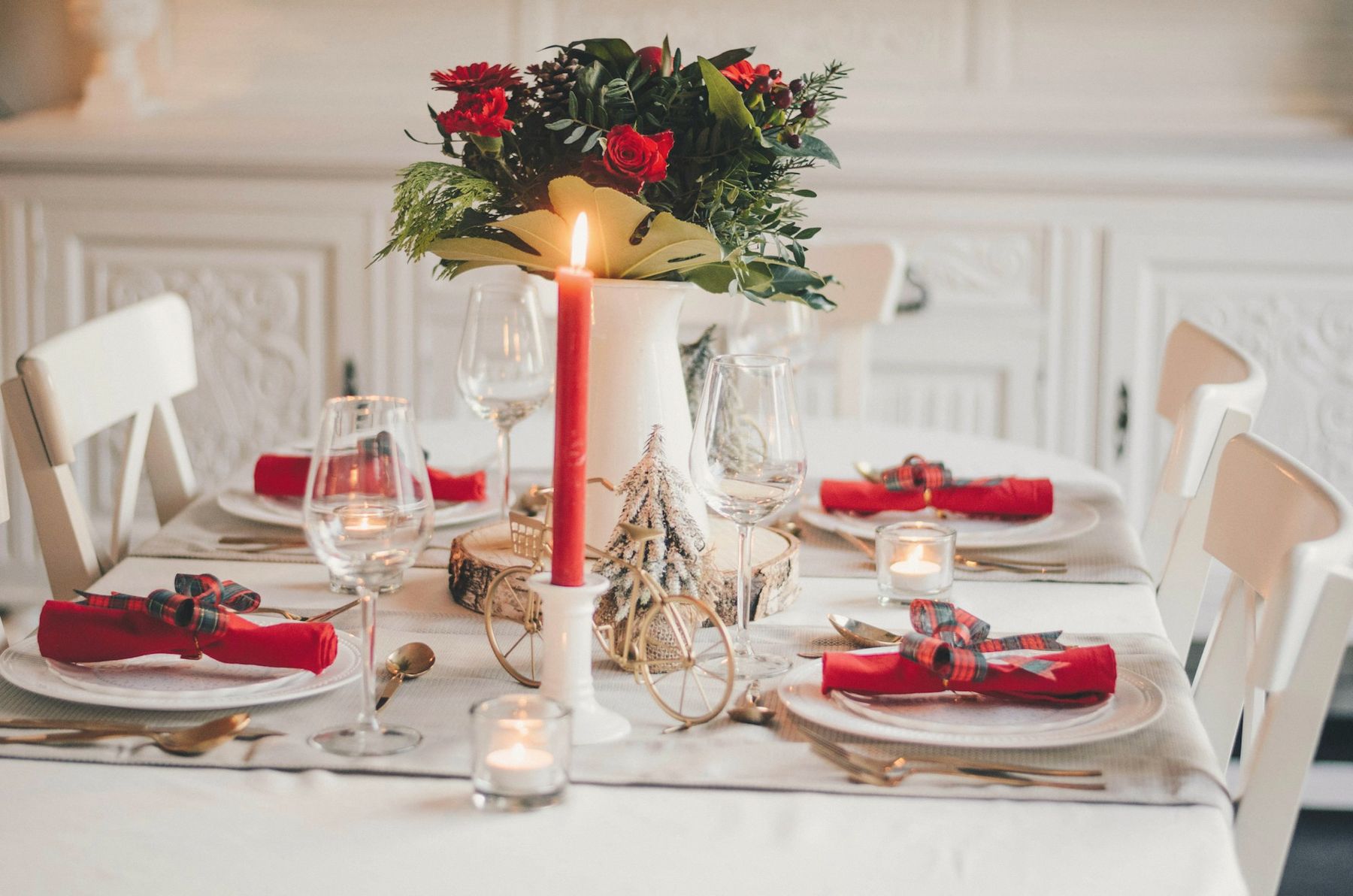 A holiday table with red napkins, candles and an evergreen centerpiece